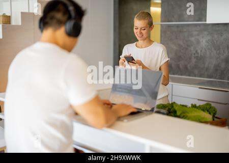 Woman cooking dish while man using laptop Stock Photo