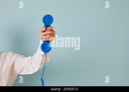 Hand of unknown man holds blue wired retro phone which is symbol of emergency call. Stock Photo