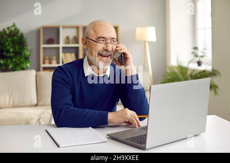 Senior business man talking on cell phone sitting in front of laptop in home office. Stock Photo