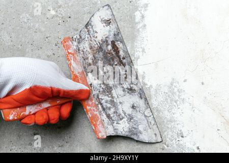 Steady hand of plasterer holding an old trowel and scrubbing concrete wall, removes old plaster during redecoration. Close-up view, selective focus on Stock Photo