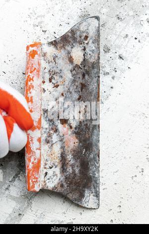 Qualified plasterer in protective glove using an old special spatula and scrapes concrete wall, removes old plaster. Home redecoration Stock Photo