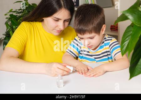 Mom applies bitter nail polish to the boy's nails to wead him from the bad habit of biting his nails Stock Photo
