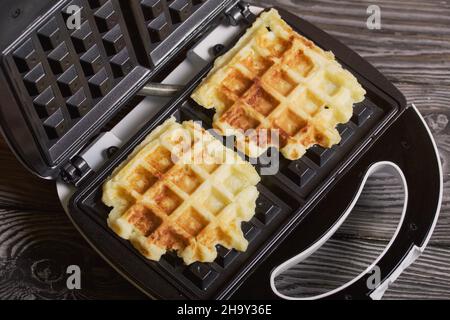 Waffle maker with waffles. On black pine boards. Close-up shot. Stock Photo