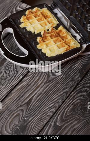Waffle maker with waffles. On black pine boards. Close-up shot. Stock Photo