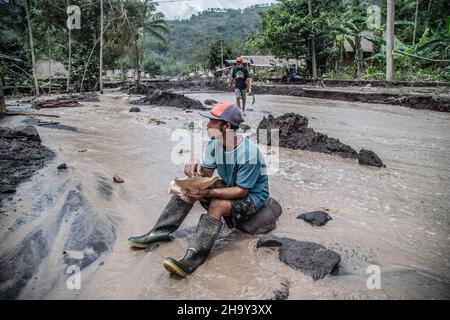 Kamar Kajang, Indonesia. 09th Dec, 2021. A villager sits on a rock amidst flowing water mixed with cold lava after the eruption of mount Semeru in Kamar Kajang, Lumajang. At least 14 people are dead and dozens are injured after Mount Semeru, a volcano in Indonesia's East Java province, erupted on Saturday, throwing towers of ash and hot clouds that covered nearby villages. (Photo by Aditya Saputra/SOPA Images/Sipa USA) Credit: Sipa USA/Alamy Live News Stock Photo