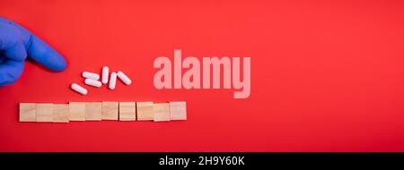 Hands in medical gloves point on wooden blocks on colored red background with medicine pills. Concept book cover medical scientific or biological temp Stock Photo