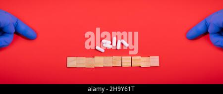 Hands in medical gloves point on wooden blocks on colored red background with medicine pills. Concept book cover medical scientific or biological temp Stock Photo