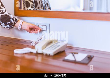 Female hand plugging in landline telephone cord into wall. Stock Photo