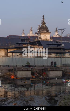 Pancha Dewal Temple across the polluted Bagmati River.  Pashupatinath Hindu temple complex in Kathmandu, Nepal.  Two cremation platforms are in front. Stock Photo