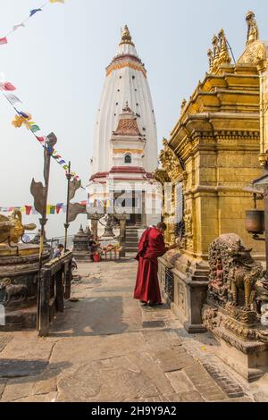 Buddhist priest worships at the Akshyobha Buddha,  on the main stupa. Swayambhunath temple complex, Kathmandu, Nepal.  Behind is the 10 Shamarpa's Bel Stock Photo