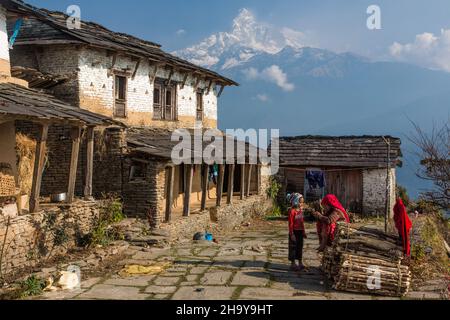 A mother and child in front of a traditional farmhouse in the Himalayan foothill village of Dhampus, Nepal.  Behind is Machhapuchare. Stock Photo