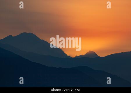The sun peaks out from behind the Mansiri Himal in the Nepalese Himalayas at sunrise, viewed from Dhampus, Nepal.  Bhauda Himal is at right. Stock Photo