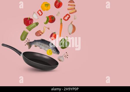 Raw trout fish with different vegetables and lemon flying above frying pan for tasty cooking, isolated on bright pink background. Minimal healthy food Stock Photo