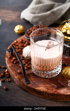 Glass of Irish cream baileys liqueur with ice, roasted coffee beans, cinnamon, Christmas decoration and chocolate on dark wood background table. Chris Stock Photo
