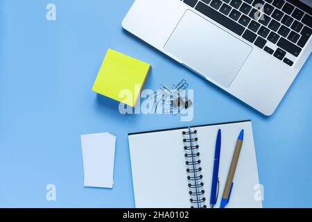 Flat lay workspace with a laptop, a notepad, and two pens, on blue background Stock Photo