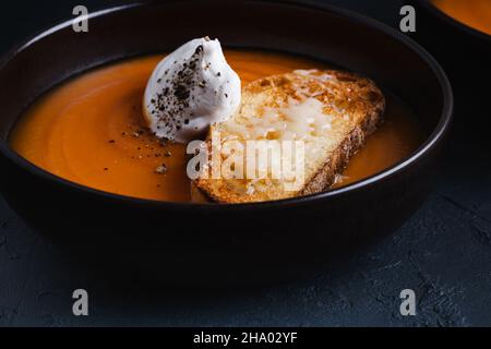Creamy butternut soup with cream, parmesan toasts in brown ceramic bowl on dark gray background, autumn cozy vegetarian dish Stock Photo