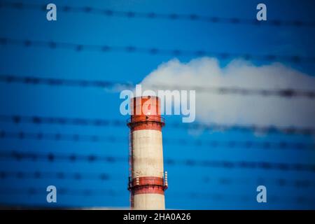 large chimney with smoke behind barbed wire Stock Photo