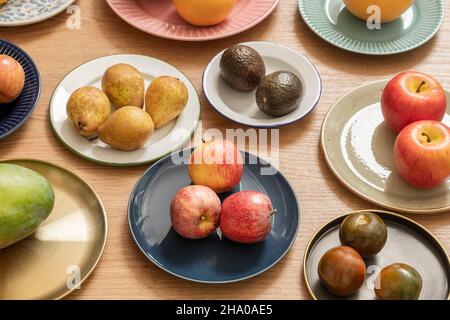 set of plates full of different fruits and vegetables on oak table, pears, avocados, tomatoes, ripe apples Stock Photo