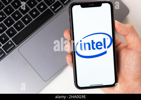 Intel mobile application on the smartphone screen. A mobile phone in a man hand near an open laptop. White background. November 2021, San Francisco, USA Stock Photo