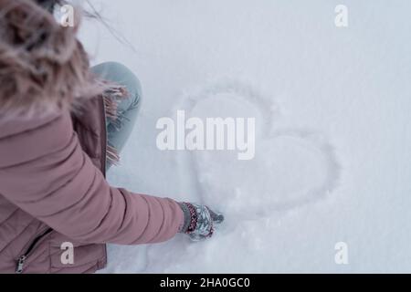 a girl in a pink jacket draws a heart in the snow,love is all around us,love melts ice Stock Photo