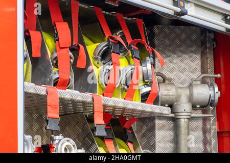 Rolled yellow hoses fastened in cells by belts with clamps in open fire truck metal body at contemporary station close view Stock Photo