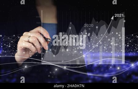 New year 2021,goal,plan,action. Hand holding digital graphic pen and drawing digital hologram growth graph chart sign on city dark blurred background. Stock Photo