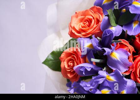 A colorful bouquet of flowers made of orange roses and purple irises. On a light background. A place to copy. The concept of the holiday. High quality photo Stock Photo