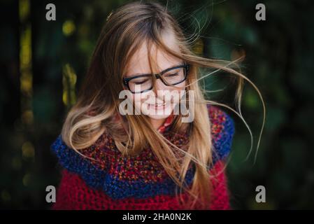 Little girl with long hair and glasses swings hair joyfully outdoors