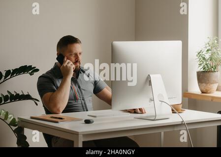 A man works remotely on a desktop computer. A guy with a beard is calling during the report of a colleague at a video conference at home. A teacher is Stock Photo