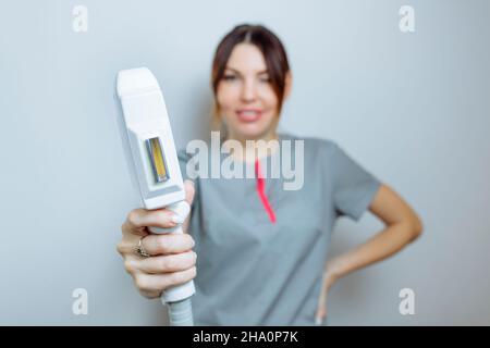 Female cosmetologist in a medical coat holds a working part of the modern laser epilator in her hands and poses for a photo. Laser epilation treatment Stock Photo