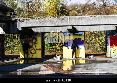 Two Young Guys spraying on Walls in an abandoned Place Stock Photo