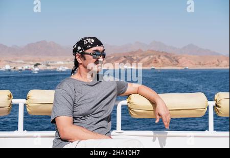 Happy senior Asian man in sunglasses and bandana traveling by boat on sea. Stock Photo