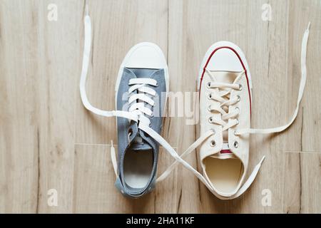 Gray and beige color casual new sneakers intertwined with white shoelaces on the wooden floor close up image. Love and friendship concept image. Stock Photo