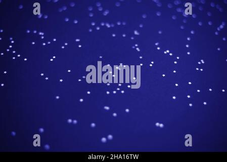 Glowing mica Silver stars confetti on blue color trendy background. Holiday confetti. Classic Flat lay. New Year 2020. Color of the year. Festive holi Stock Photo