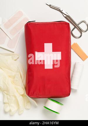 Red first aid medical kit bag with scissors, tape and gloves top view flat lay from above over white background Stock Photo
