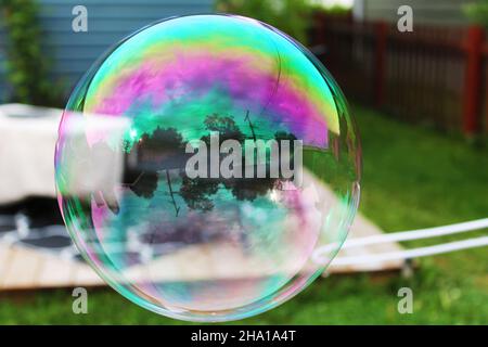 Closeup of a large bubble outside, garden in background and reflected in bubble. Stock Photo