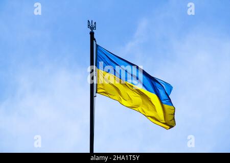 Ukrainian flag in the rays of the rising sun on a background of sky. Bicolor blue and yellow national flag of Ukraine on a flagpole and coat of arms Stock Photo