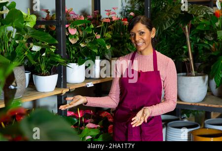 Woman florist standing among shelves with flowers and plants Stock Photo