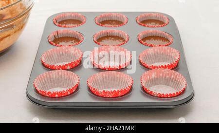 Muffin pan with paper cupcake liners close up on kitchen table. Step by step chocolate muffins recipe, baking process Stock Photo