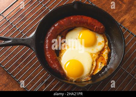 Fried eggs with sausage on frying pan close up on wooden background Stock Photo
