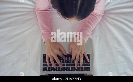 Hands of woman typing on laptop keyboard on bed. Stock Photo