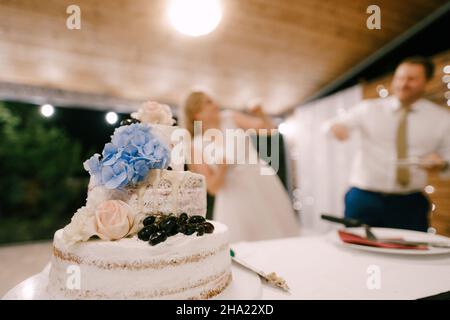 Three-tiered wedding cake stands on the table against the background of dancing guests Stock Photo