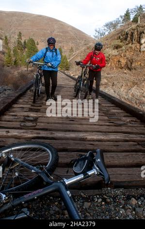 Two women cross bridge with mountain bikes. Oregon