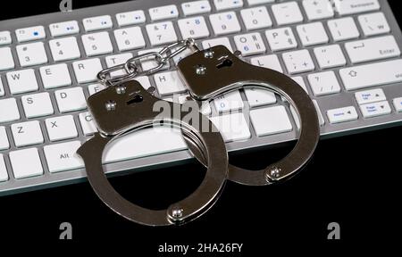 Keyboard and handcuffs with LED lights on. Cybercrime concept Stock Photo
