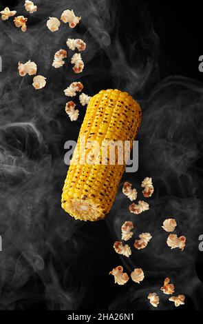 Grilled ear of corn and popcorns hovering in smoke on black background Stock Photo