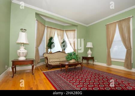 Interior room, family, living room with sofa, coffee and end tables, lights, curtains on windows. Light green walls and shiny wood floor. Stock Photo