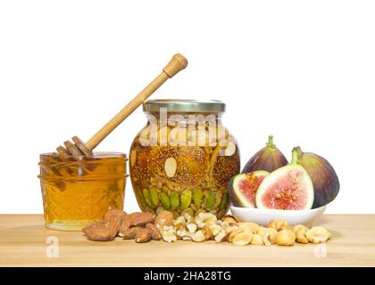 Jar of nuts and fruit preserved in a jar of honey. Ingredients Pistachios, walnuts, peanuts, almonds and figs on a light wood table isolated on white. Stock Photo