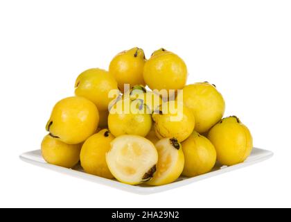 Small square porcelain plate piled high with fresh ripe lemon guava fruit, isolated on white. One fruit sliced in half on front of plate. Stock Photo