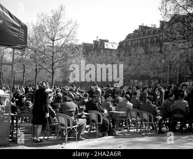 Sidewalk cafe along the Champs-Elysees,1945. One of two photographs that depict the same sidewalk café located perhaps near the George V Metro. It is crowded to capacity and many of the customers are clearly American or British military. It is a sunny day and the trees display early spring foliage. There are many pedestrians on the street. The mood is what you would expect for a fine spring day with the Occupation a recent memory. In this photograph, Stock Photo