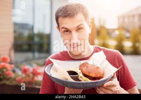 A funny man licks his lips and leers at a fresh delicious and greasy burger. Junk and street food concept Stock Photo